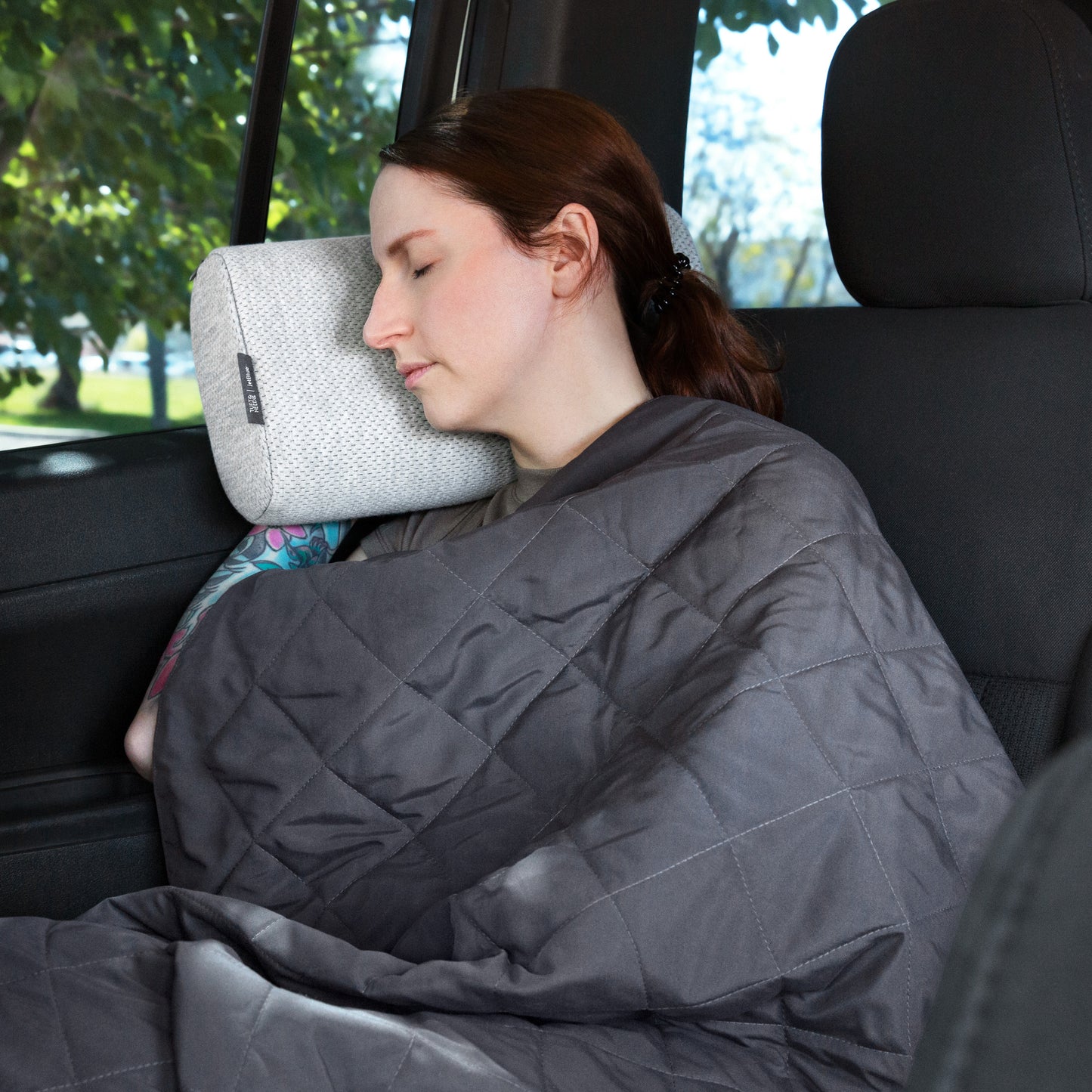 A woman sleeping in a car on the Tuft and Needle Anywhere Travel pillow ||color:granite